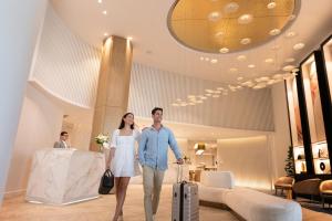 a man and woman walking through a hotel lobby with their luggage at Dorsett Gold Coast in Gold Coast