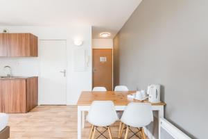 cocina y comedor con mesa de madera y sillas blancas en Appart'hotel Victoria Garden Pau, en Pau