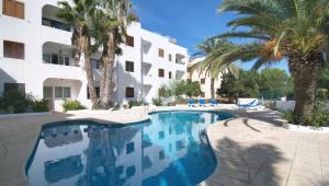 a swimming pool in front of a building with palm trees at Apartamentos Costamar II in Es Pujols