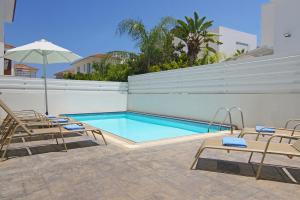 a swimming pool with chairs and an umbrella at Villa Paloma in Paralimni