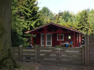 a red cabin in the woods behind a fence at Vakantiewoning Hegga in Hegelsom