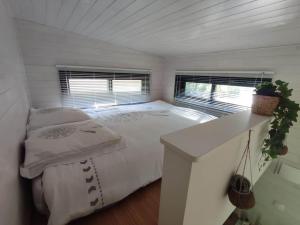 a white bedroom with a bed and two windows at Tiny house chez Caroline in Gaillan-en-Médoc