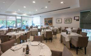 a dining room with white tables and chairs and windows at Sercotel Riscal in Puerto Lumbreras