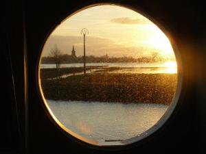 een uitzicht op de zonsondergang door een rond raam bij De Boot in Merkem