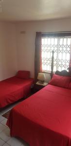 twee bedden in een kamer met rode lakens en een raam bij Montego Bay westgate Hills jamaica Melrose place in Montego Bay