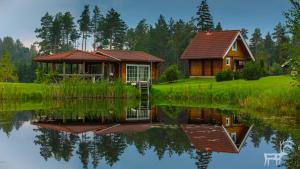 a cabin on the shore of a lake with its reflection in the water at Viesu mājas Briedīši in Raiskums