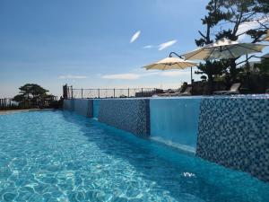 a blue swimming pool with an umbrella and chairs at Villa de Aewol in Jeju