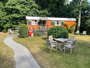 an orange trailer with a table and chairs in a yard at Zirkuswagen am Landhaus Labes (Stechlinsee) in Neuglobsow