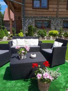 eine Terrasse mit 2 Korbstühlen und einem Tisch mit Blumen in der Unterkunft Magurskie Bywanie in Witów
