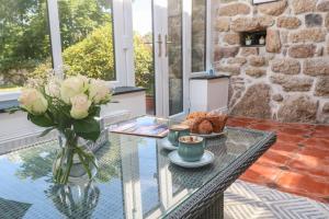 a glass table with a vase of roses and a vase of food at Trevedran Cottage in Penzance