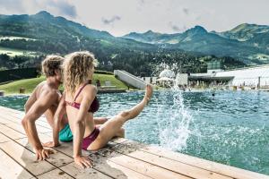 un garçon et une fille assis sur un quai près d'une piscine dans l'établissement KENDLGUT Appartements am BioBauernhof inklusive unbegrenztem Eintritt in die Alpentherme, à Bad Hofgastein
