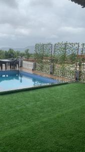 een zwembad met groen gras en een hek bij THE DECK in Karjat