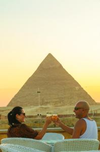 a man and a woman holding glasses in front of the pyramids at Pyramids Valley Boutique Hotel in Cairo