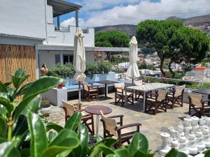 un patio con mesas, sillas y sombrillas blancas en Villa Arni Andros - Βίλα ΑΡΝΗ, en Batsi