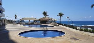 a swimming pool next to the ocean with palm trees at Marazú OndinaApart in Salvador