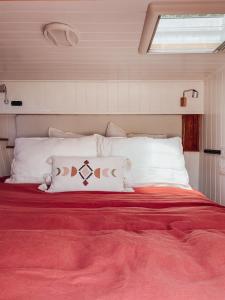 ein Bett mit weißen Kissen und einer roten Decke in der Unterkunft Relaxing retreat for 2 on beautiful converted bus in Levaré