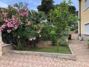 Appartamento 150 mq in villa sul mare a Fertilia في فيرتيليا: حديقة بها زهور وردية على رصيف من الطوب