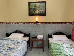 two beds in a room with a table and a painting at Pondok Batur Indah Homestay Karangasem in Tirtagangga