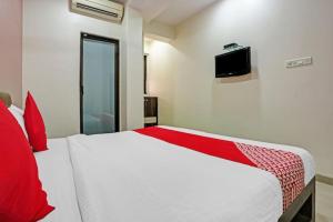 Hotel Amfahh - Andheri West Railway Station في مومباي: غرفة نوم بسرير ابيض ومخدات حمراء وتلفزيون