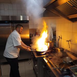 Ein Mann in einer Küche mit einem Feuer in einer Pfanne. in der Unterkunft Gastland M1 Hotel & Conference Center in Páty