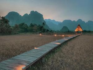 een houten loopbrug in een veld met bergen op de achtergrond bij ViengTara VangVieng Resort in Vang Vieng