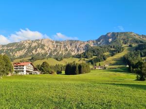 a house in a field with mountains in the background at Bergzeit - Hotel & Appartements in Oberjoch