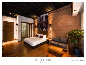 ein Schlafzimmer mit einem Bett, einer Couch und einer Backsteinwand in der Unterkunft The Loft Hotel Downtown Yangon in Yangon