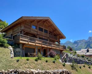 una casa di tronchi su una collina con montagne sullo sfondo di CHALET LYOBA a Le Grand-Bornand