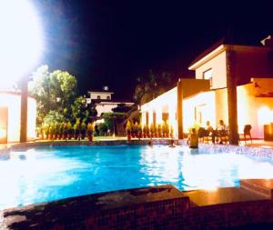 uma grande piscina à noite com pessoas sentadas à sua volta em StayApart - Aasmaa Farm Stay em Ābādpura