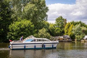 a man is standing on a boat in the water at Morea Cottage - 2 Bed in Horning