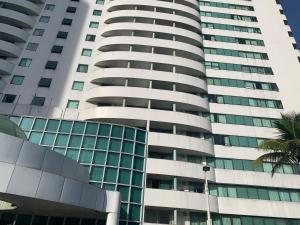 Lindo Flat na Barra da Tijuca com vista para o mar في ريو دي جانيرو: مبنى طويل يوجد أمامه شجرة نخيل