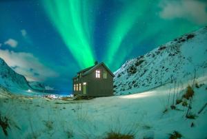 a cabin under the northern lights in the snow at Feriehus med flott havutsikt ved Hauklandstranden in Leknes