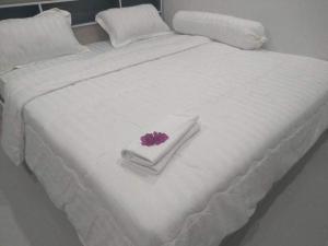 Una cama blanca con una flor morada encima. en บ้านบัวหลวงกันตังเมืองเก่า, en Ban Laem Muang