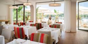 un comedor con mesas y sillas blancas y ventanas en Hotel Supetar en Cavtat