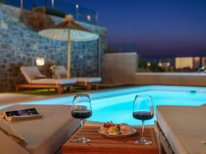 dwa kieliszki wina i talerz jedzenia obok basenu w obiekcie Ligaria Mare w mieście Agia Pelagia