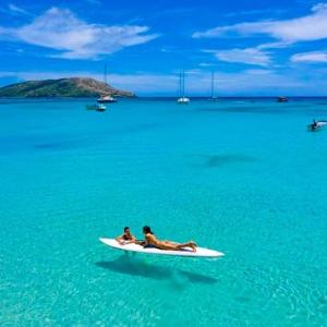 due persone sedute su una tavola da surf in acqua di Nabua Lodge a Nacula Island