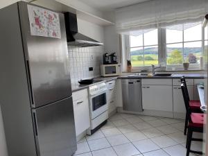 una cocina con nevera de acero inoxidable y armarios blancos en Ferienwohnung-Orth-Tor-zum-Sauerland-mit-grosser-Terrasse en Meinerzhagen
