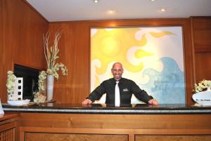 een man in een stropdas zittend aan een toonbank bij Hotel Galleano in Marina dʼAndora