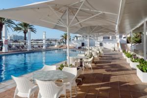 an outdoor patio with tables and chairs and a pool at AluaSun Lago Park in Cala'n Bosch