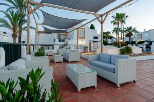a patio with couches and tables and palm trees at AluaSun Lago Park in Cala'n Bosch