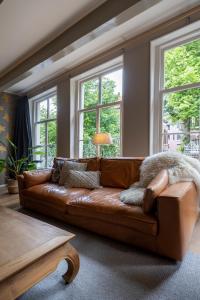 a brown leather couch in a living room with windows at Royal City Suite Monsieur Philippe in Leeuwarden