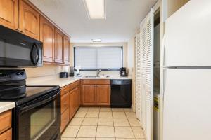 a kitchen with wooden cabinets and a black refrigerator at 2-Bedroom Carolina Dunes Condo with Private Balcony and Ocean Views in Myrtle Beach