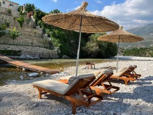 River Escape Villa - Private Beach, Scenic view & BBQ في Tepelenë: مجموعة من الكراسي والمظلات على الشاطئ
