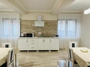 a kitchen with white cabinets and tables and windows at M House Băile Herculane in Băile Herculane