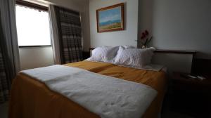 a bedroom with a bed with white sheets and a window at Apartamento em frente ao mar Praia da Costa in Vila Velha