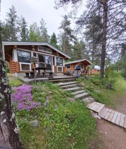 a cabin in the woods with purple flowers in front of it at Hirsimökki ja makuuaitta in Karijoki