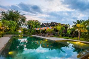 ein Pool mit Sonnenschirmen vor einem Haus in der Unterkunft Phum Khmer Lodge - Village Cambodian Lodge in Siem Reap