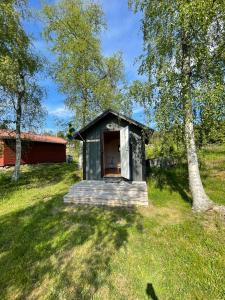 una piccola casa nera in un campo con un albero di Tynderösundet - Gråstugan 