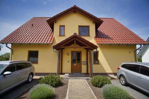 ein gelbes Haus mit rotem Dach und zwei geparkten Autos in der Unterkunft Schicke FeWo mit Terrasse, gratis Nutzung vom AHOI Erlebnisbad und Sauna in Sellin - Haus De niege Wech FeWo 01 in Thiessow