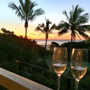 Dois copos de vinho sentados numa varanda a ver o pôr-do-sol. em Mooloomba Two em Point Lookout